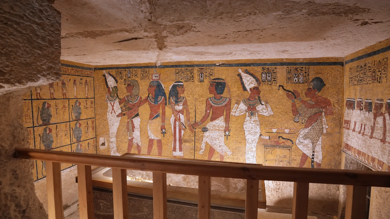 Parois peintes de la chambre funéraire de Toutankhamon, avec personnages, hiéroglyphes et babouins sur fond jaune.